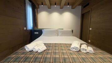 A hotel room with a plaid bedspread, neatly folded towels, and wooden walls.