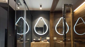 Un baño moderno con un lavamanos central de mármol, cabina de ducha con paredes de vidrio y detalles de madera.