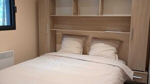 A bedroom with a bed, built-in wooden shelving, a window, and a radiator. - New 2CH gîte with private pool - Peace, nature & comfort 10min from Bergerac (Lembras)