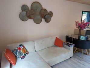 A living room with a sofa, decorative wall art, a small table with a vase of flowers, and a window with a view. - New 2CH gîte with private pool - Peace, nature & comfort 10min from Bergerac (Lembras)