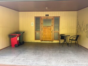 Una habitación con una puerta de madera, dos sillas, una mesita y dos cubos de basura.