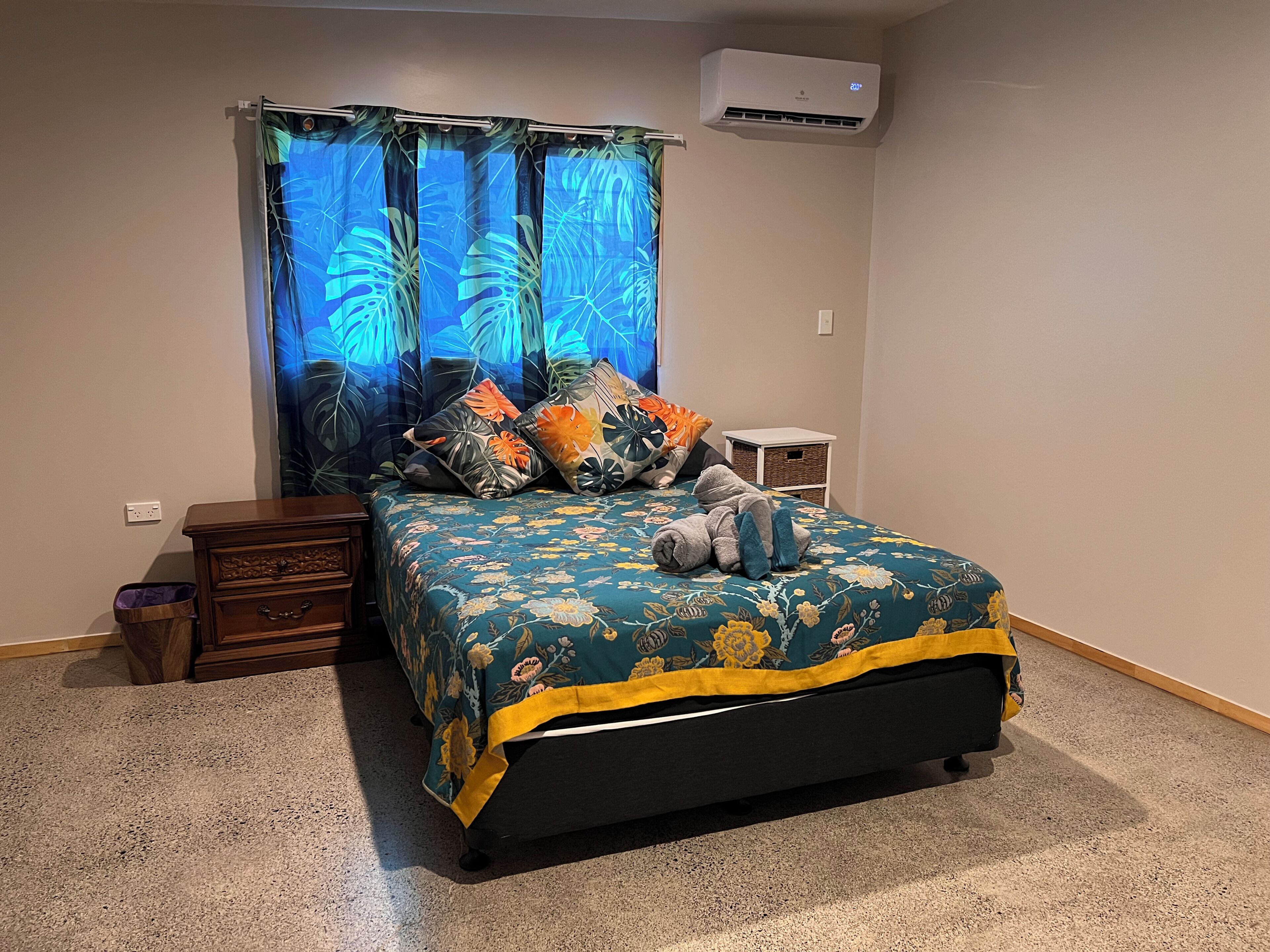 Een slaapkamer met een bed, nachtkastje, klein tafeltje en een airconditioning.
