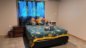 Een slaapkamer met een bed, nachtkastje, klein tafeltje en een airconditioning.