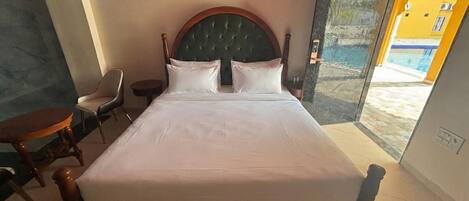 Een hotelkamer met een bed, een stoel, een klein tafeltje en uitzicht op een zwembad.