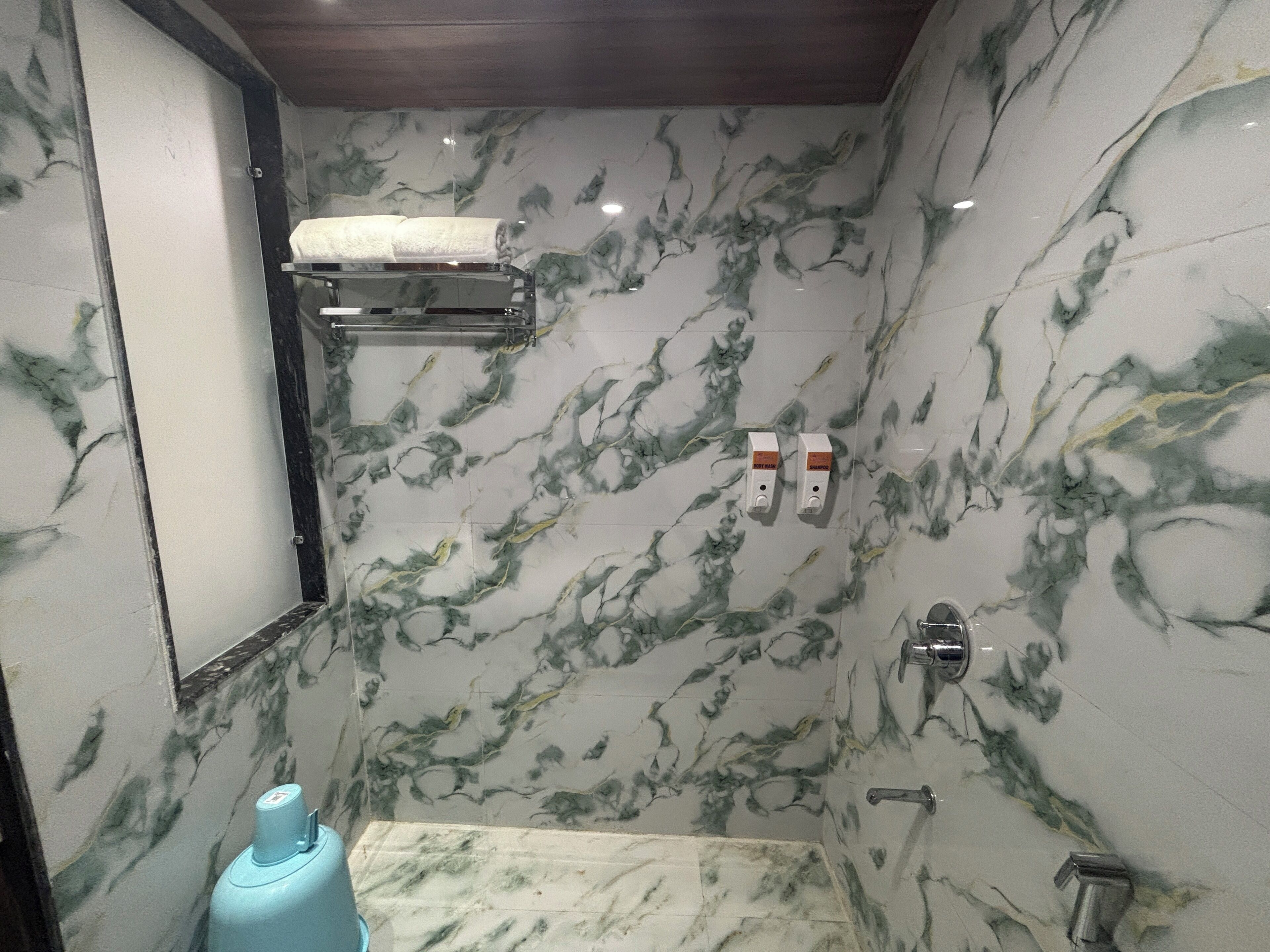 A bathroom with marble walls, a towel rack, a soap dispenser, and a shower area.