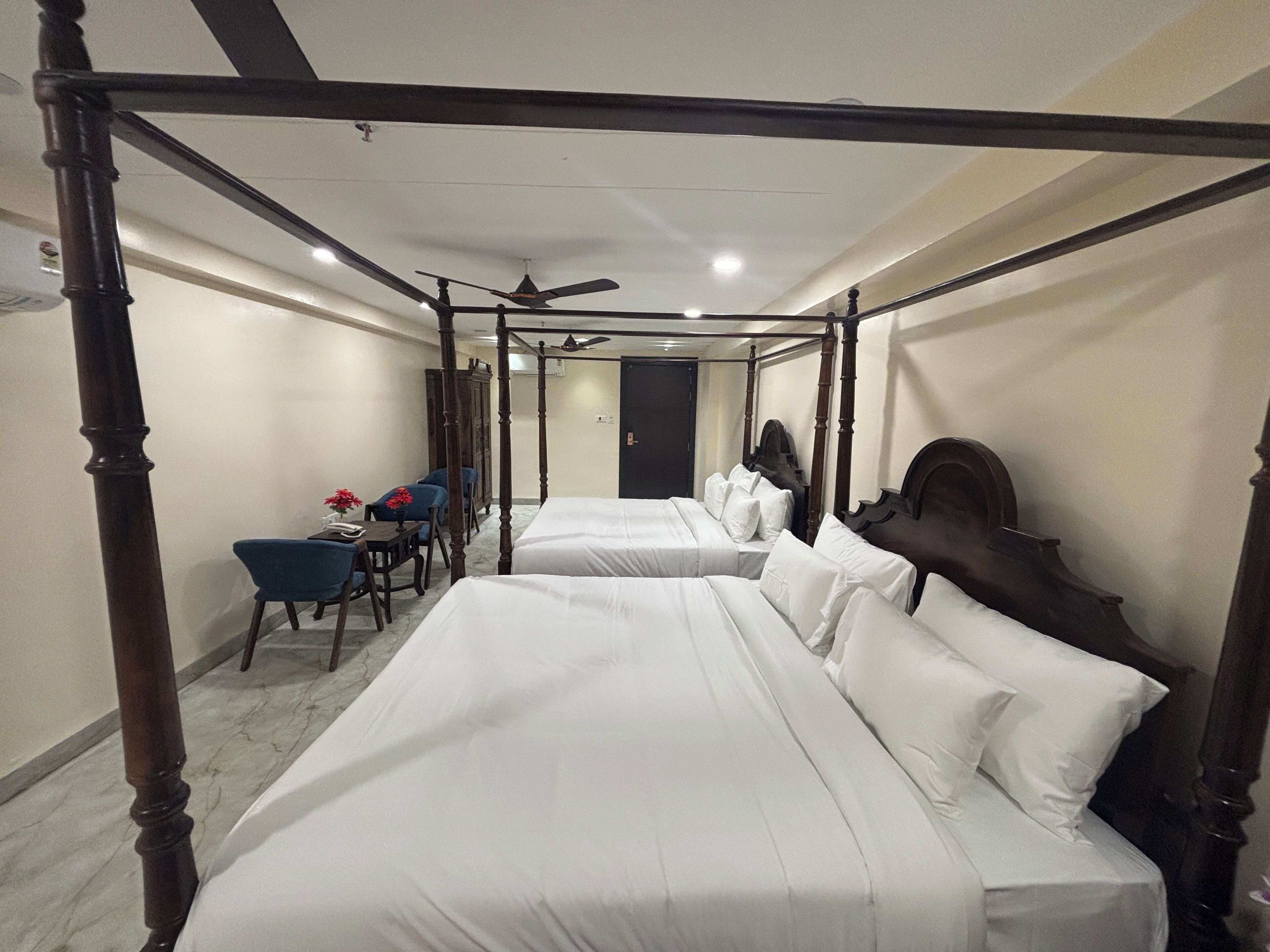 A four-poster bed room with two beds, a desk, and chairs.