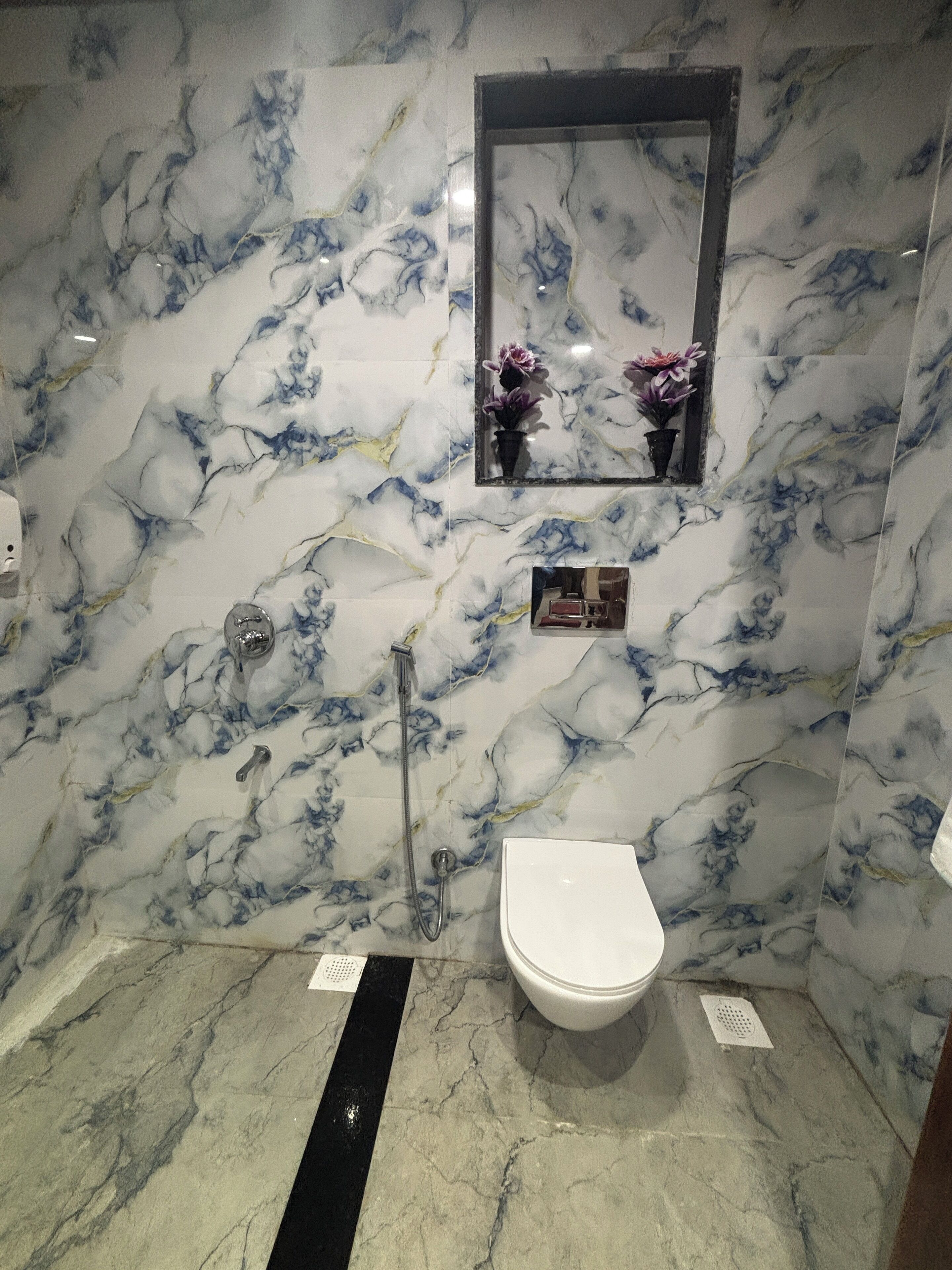 Une salle de bain avec des toilettes blanches, une douche et un mur en marbre.