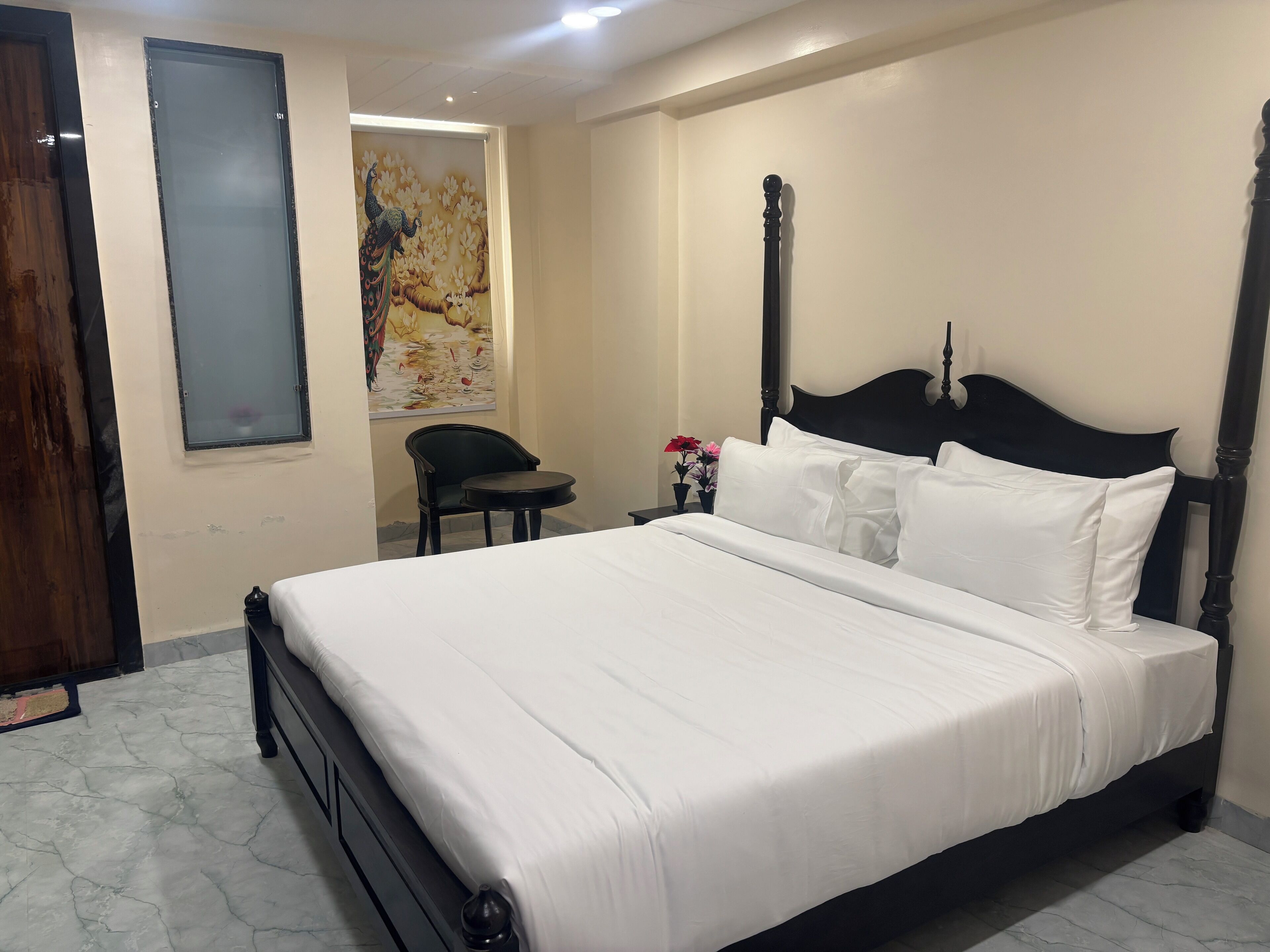 A neatly made bed with white linens in a room with a marble floor, a wooden door, and a painting on the wall.