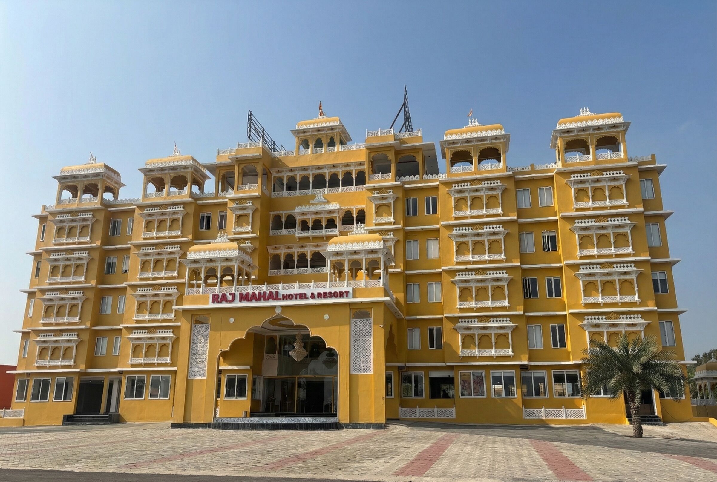 A large, yellow building with multiple balconies and a sign reading "RAJ MAHAL HOTEL & RESORT".