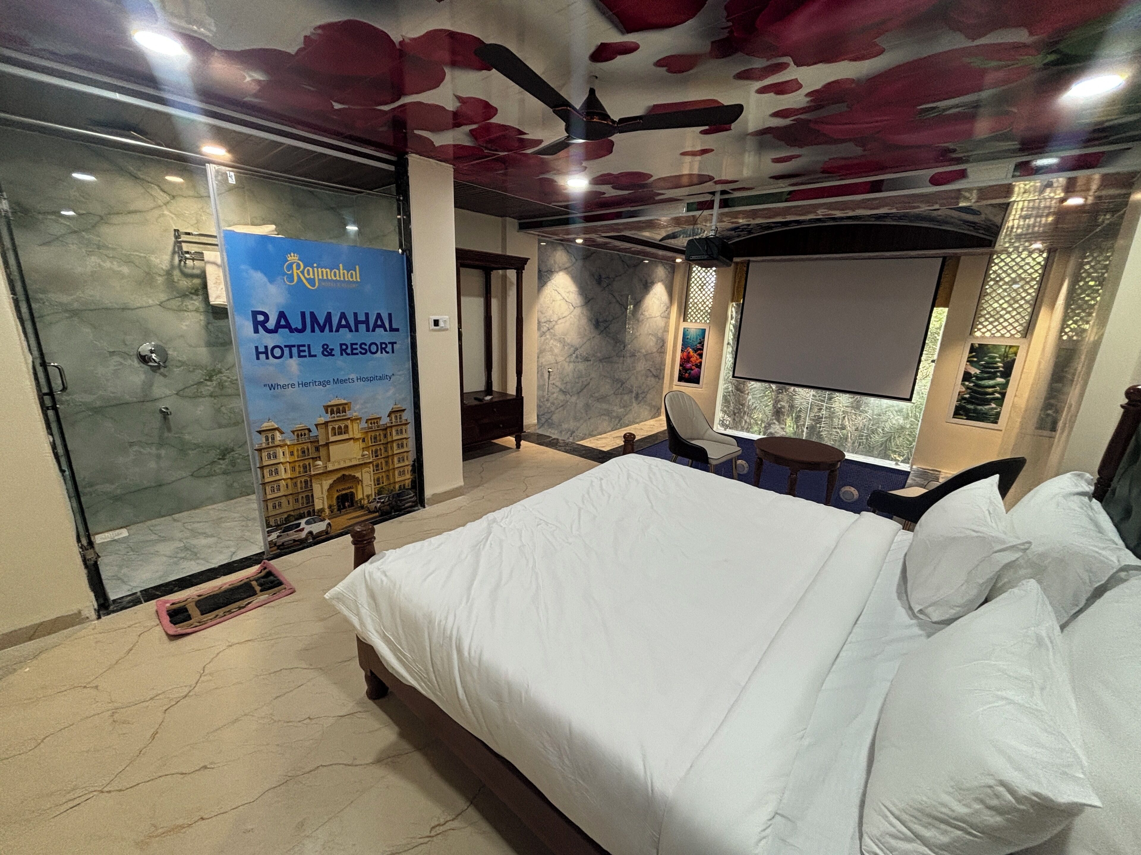 A hotel room with a bed, a shower, a seating area, and a large poster of the hotel.