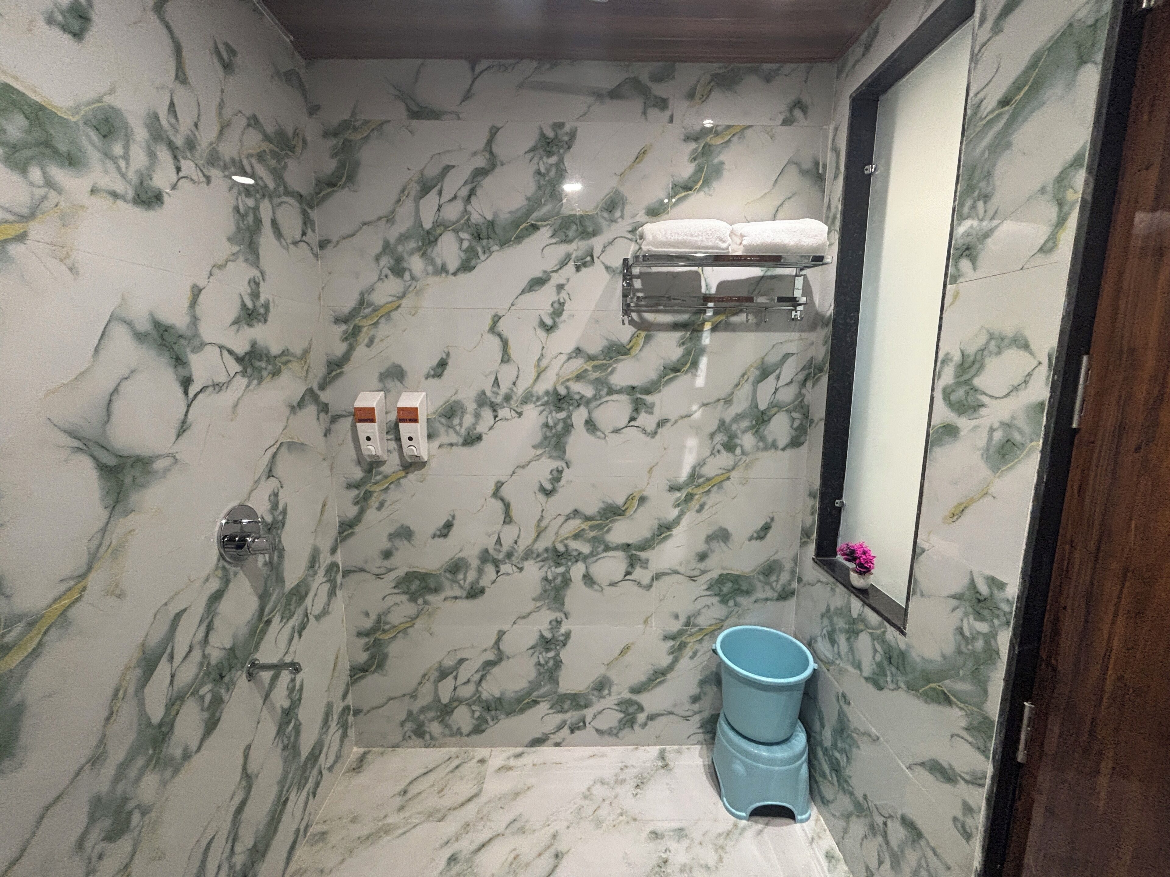 A bathroom with marble walls, a toilet, a blue trash bin, and a towel rack with towels.