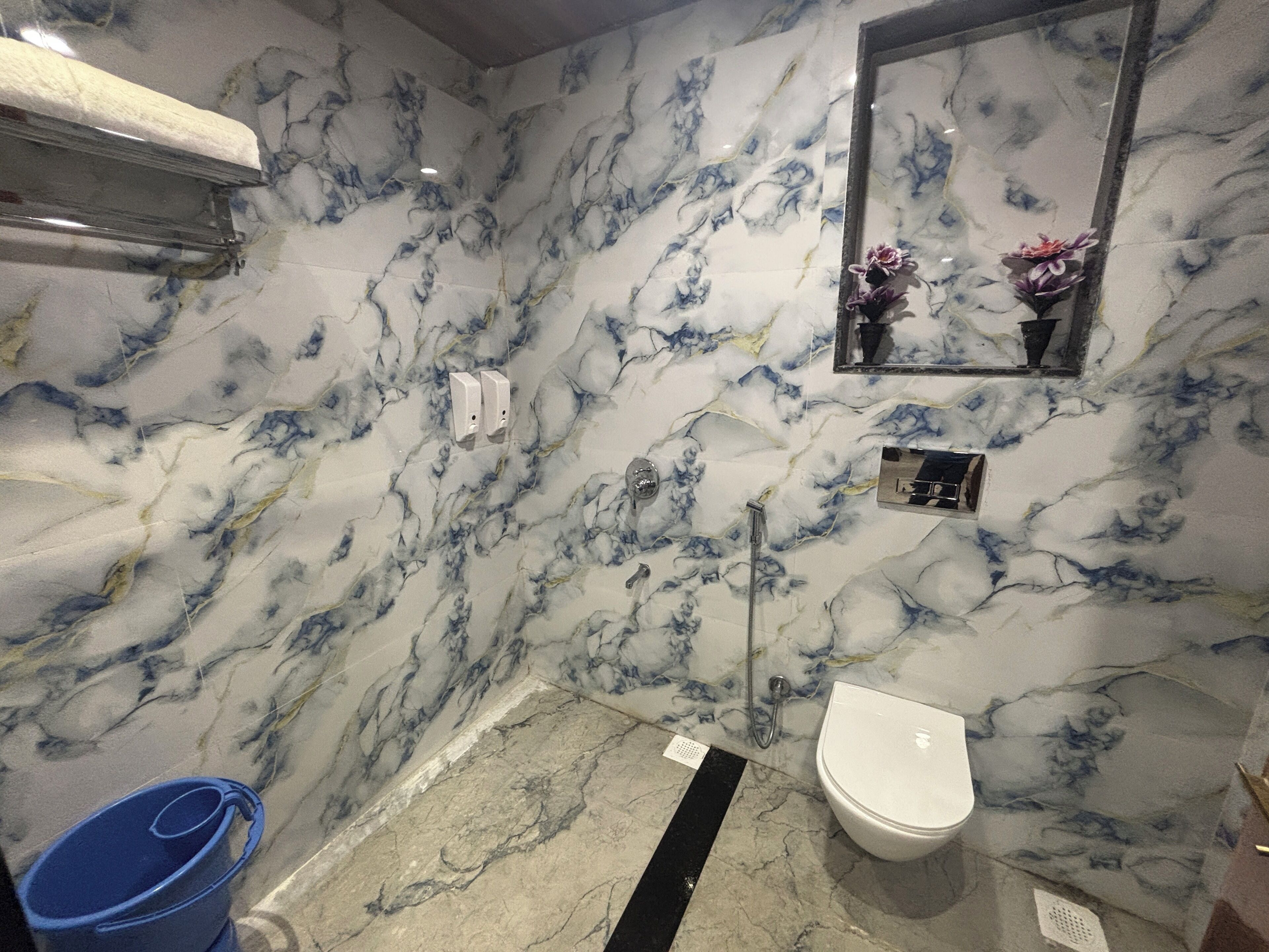 A bathroom with marble walls, a white toilet, a shower, and a blue bucket.