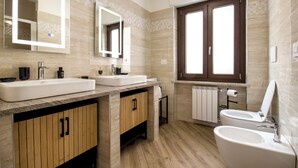 A modern bathroom with two sinks, a toilet, and a bidet. It features wooden cabinets, a large mirror, and a window with blinds. - Sonia Holiday Home - Jessica Apartment combines intimacy comfort and coziness (Pont-Saint-Martin)