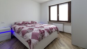 A bedroom with a bed, a nightstand, a window, and a radiator. - Sonia Holiday Home - Jessica Apartment combines intimacy comfort and coziness (Pont-Saint-Martin)
