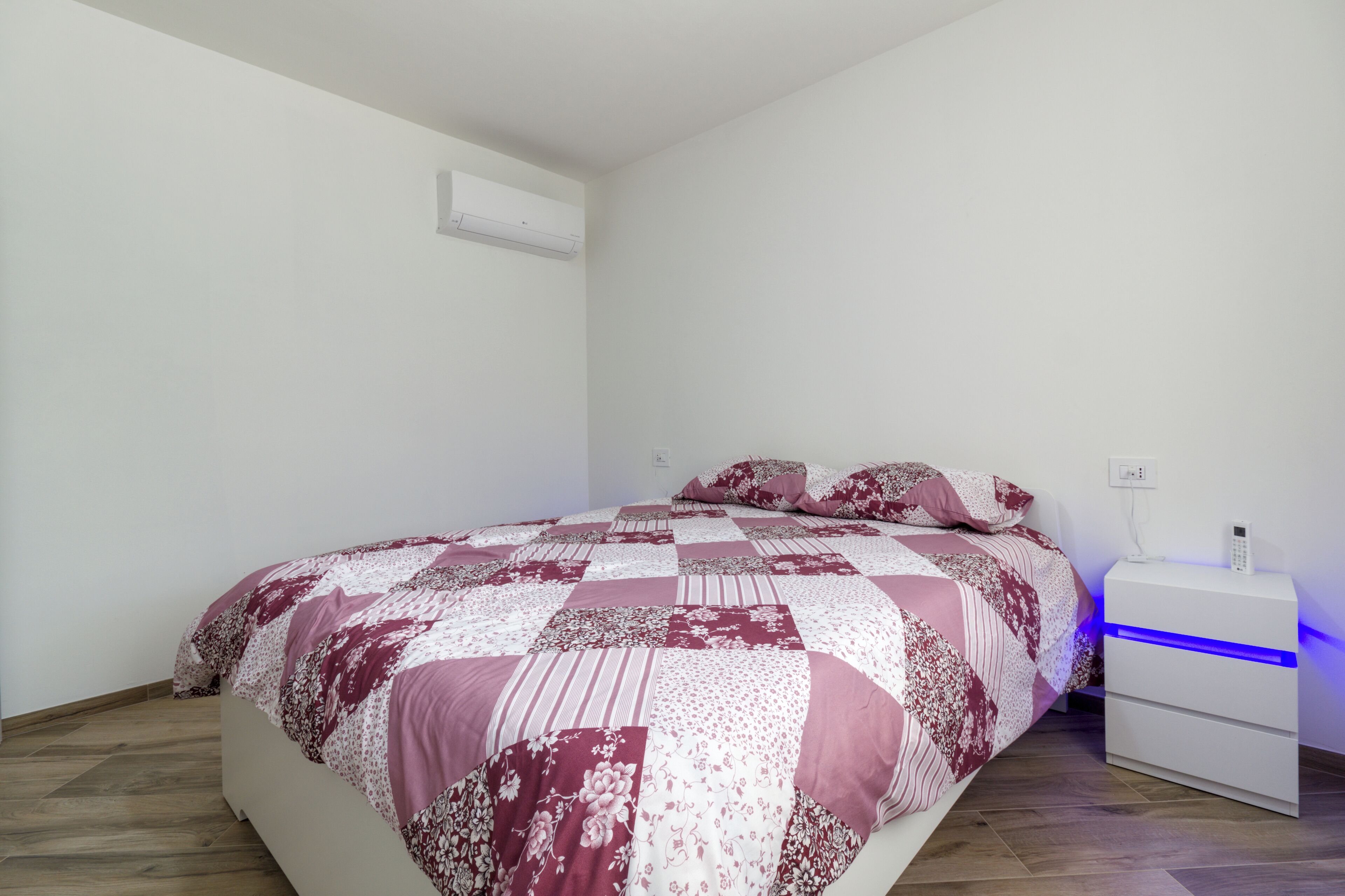A bedroom with a large bed, a bedside table with a phone, and a wall-mounted air conditioner.