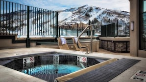 Un espace avec un bain à remous offrant une vue sur les montagnes enneigées, une piscine avec des indications de profondeur et un mur en pierre.