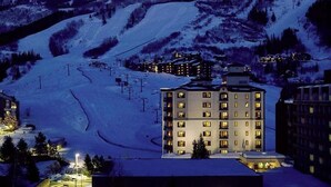 Une montagne enneigée, avec une station de ski et un hôtel à plusieurs étages dont les fenêtres sont illuminées.