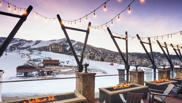 Un espace extérieur aménagé avec des foyers et des chaises, offrant une vue sur un paysage enneigé et une station de ski.