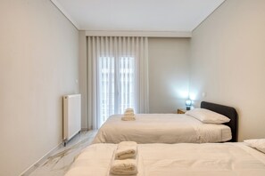 Ett hotellrum med två sängar, ett element, ett fönster med gardiner och ett nattduksbord med en lampa.