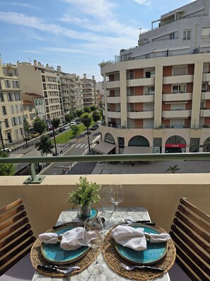 A balcony with a table set for two, overlooking a cityscape with multi-story buildings and a street. - Beach Studio, Nice, France (Nice)