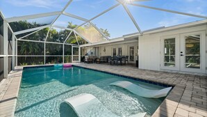 Una piscina con cerramiento de vidrio, rodeada por un patio amoblado.
