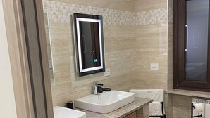 Ein modernes Badezimmer mit zwei Waschbecken, einem beleuchteten Spiegel, Holzschränken und einer gefliesten Rückwand.