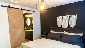 A bedroom with a bed, a nightstand, a wall-mounted macrame decoration, and a sliding door leading to a bathroom. - Townhouse - 2 bedrooms, both ensuites! (Red Deer)