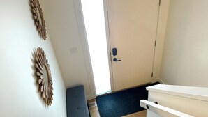 A hallway with a white door, a bench, and two wall-mounted wooden decorations. - Townhouse - 2 bedrooms, both ensuites! (Red Deer)