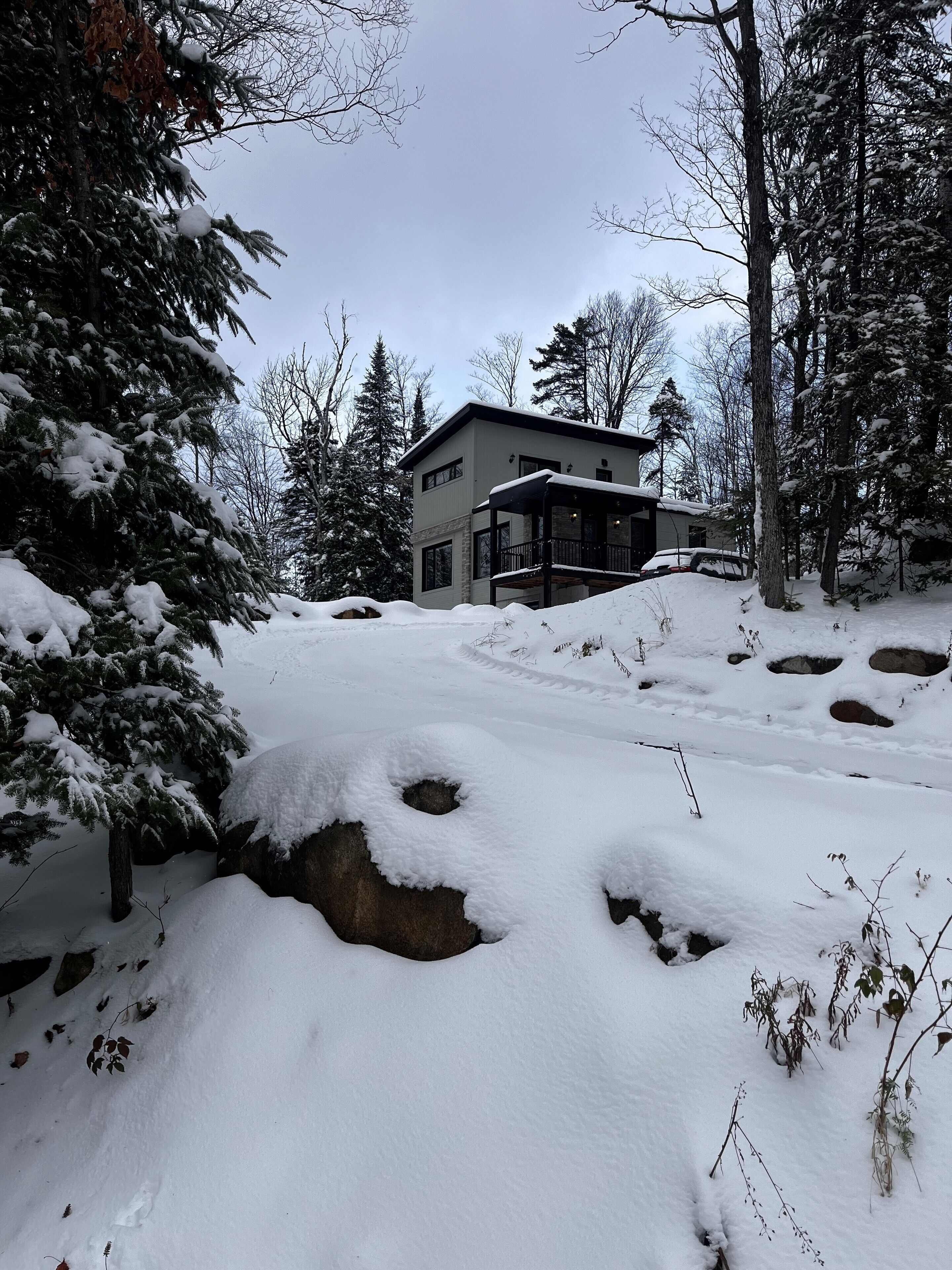 Una casa moderna de dos pisos rodeada de árboles cubiertos de nieve y un cielo despejado.