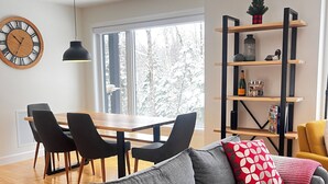 Moderni olohuone, jossa on harmaa sohva, mustat tuolit, puinen ruokapöytä ja kirjahylly.