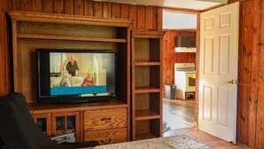 Una habitación con televisión, estanterías de madera, una puerta y una zona de cocina.