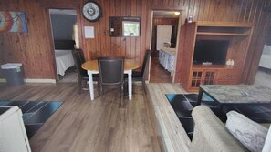 Un intérieur en bois comprenant une table à manger, des chaises, un canapé, un téléviseur et un petit coin cuisine.