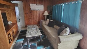 Una sala de estar con un sofá, una mesa de centro, una lámpara y un cartel en la pared.