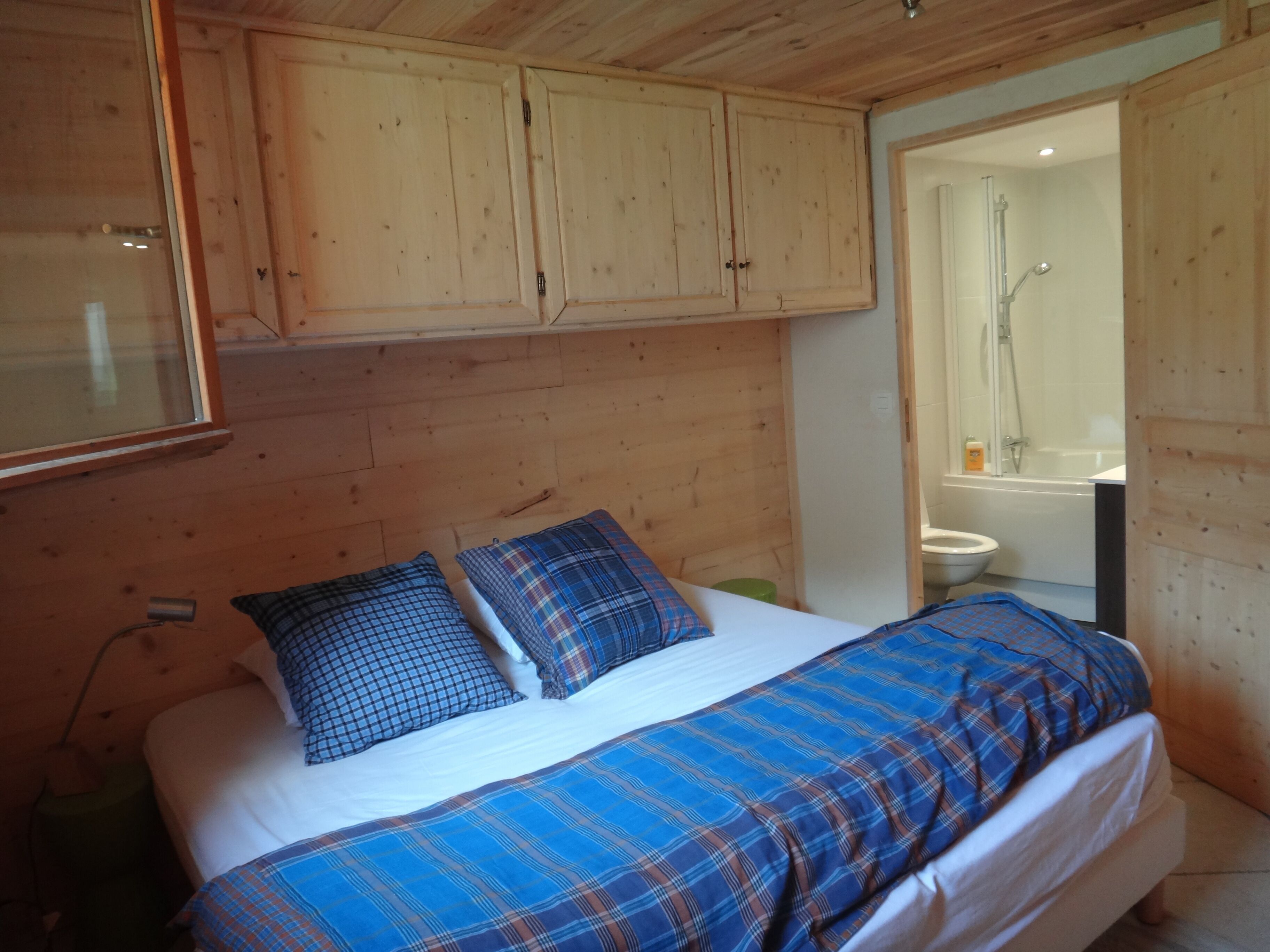 Un dormitorio estilo cabaña de madera con una cama, dos almohadas y un baño visible a través de una puerta abierta.