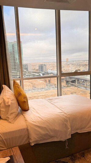 A bed with white bedding, a brown headboard, and a view of a cityscape through large windows. - Lambert Hotel (Riyadh)