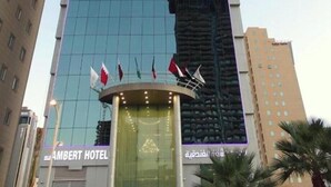 Ein hohes Hotelgebäude mit moderner Glasfassade, einem markanten Eingangsbereich und der Aufschrift "AMBERT HOTEL".