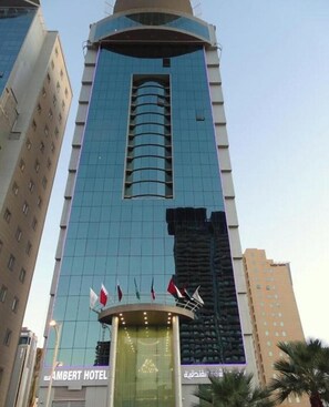 Un edificio de hotel alto con fachada de vidrio moderna, una entrada destacada con banderas y el nombre 'AMBERT HOTEL'.