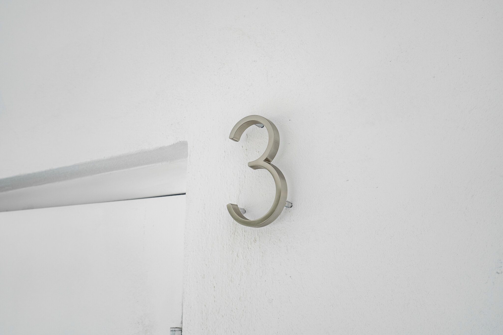 Un chiffre « 3 » en métal, fixé sur un mur blanc.