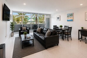 A modern living room with a black leather sofa, a dining table with chairs, and a flat-screen TV mounted on the wall. - BeachSide 9th Residences (Fort Lauderdale)