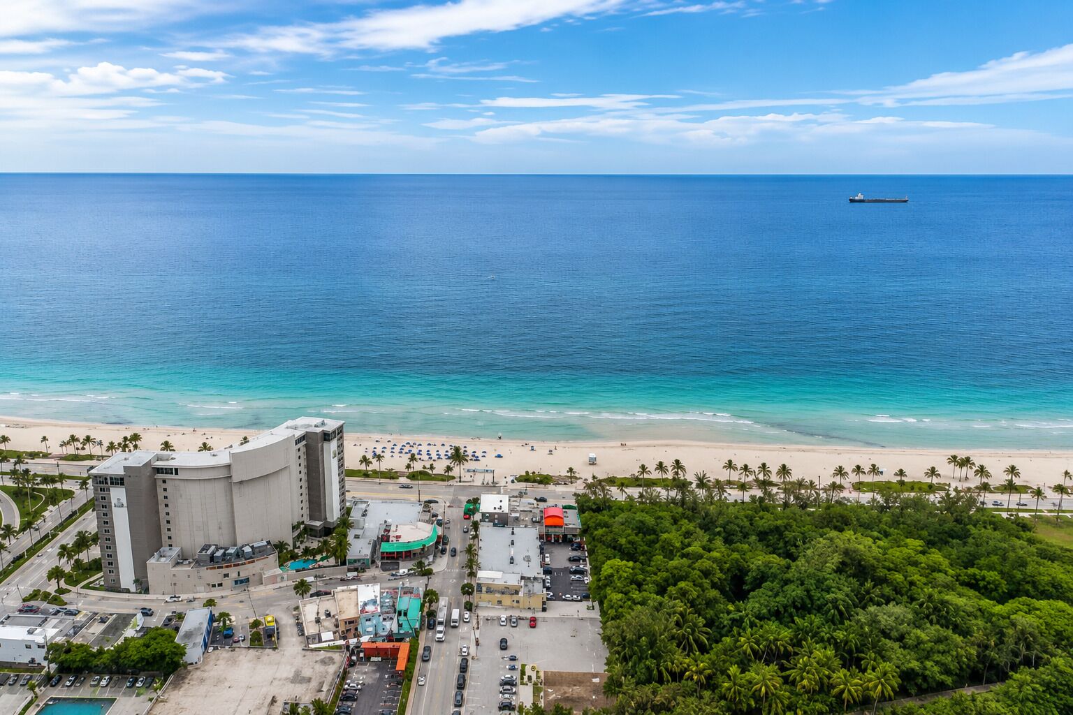 A coastal cityscape with a beach, a large building complex, and a ship in the distance.
