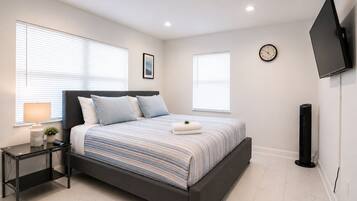 Ein modernes Schlafzimmer mit Bett, Nachttischen, einem Wand-Fernseher und einer Uhr.