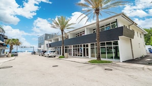 A modern building with large windows and a flat roof, surrounded by palm trees and parked cars. - BeachSide 9th Residences (Fort Lauderdale)