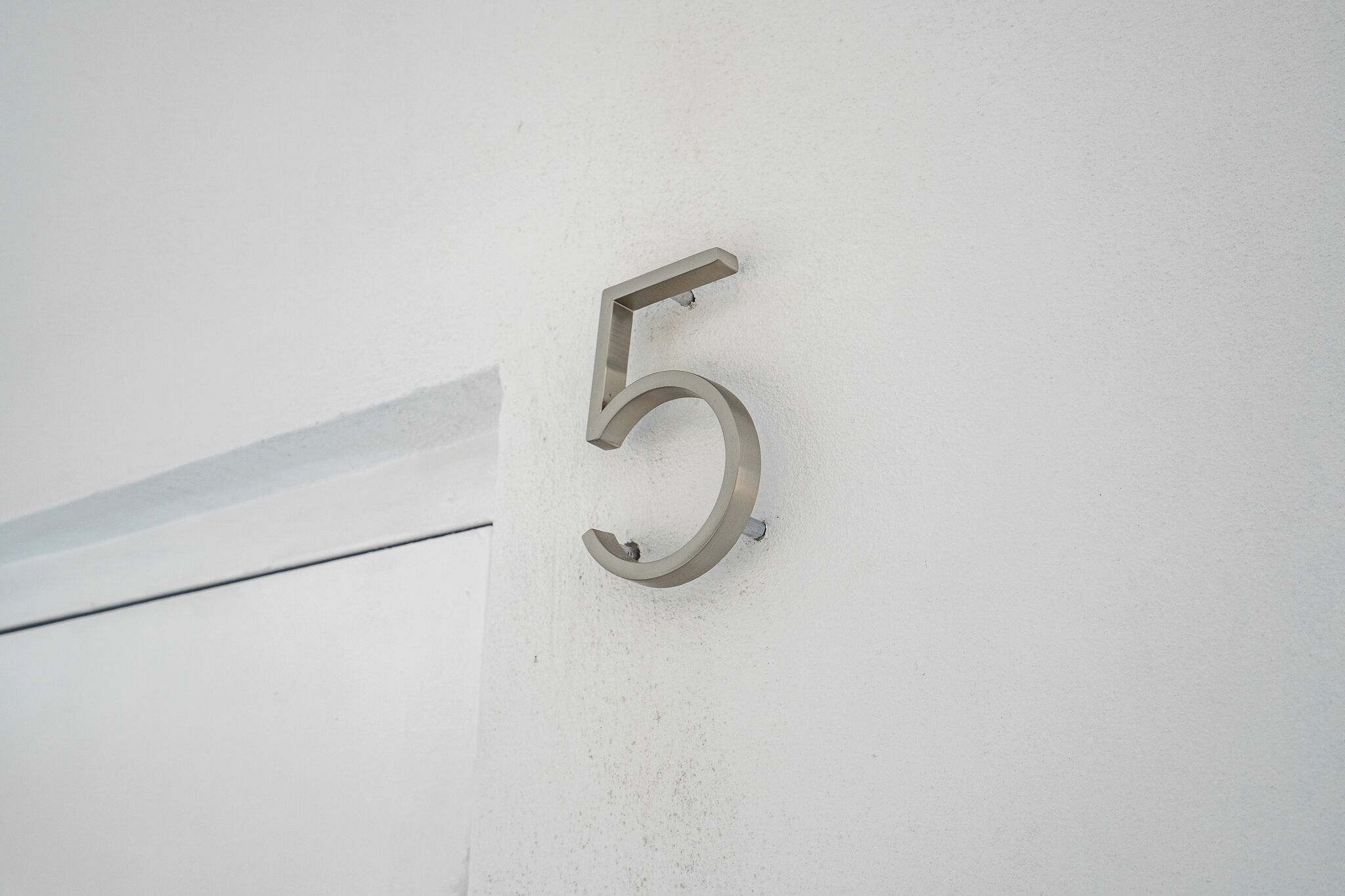 Número 5 metálico fixado em parede branca.