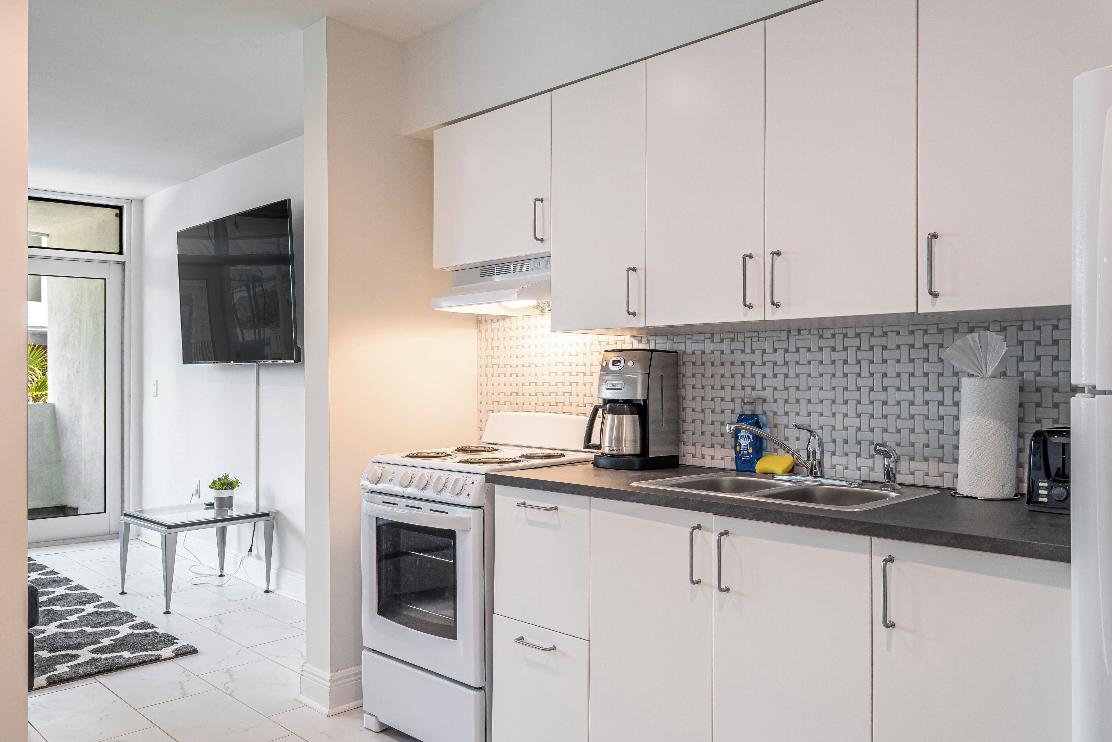 A modern kitchen with white cabinets, a built-in oven, a coffee maker, and a sink.