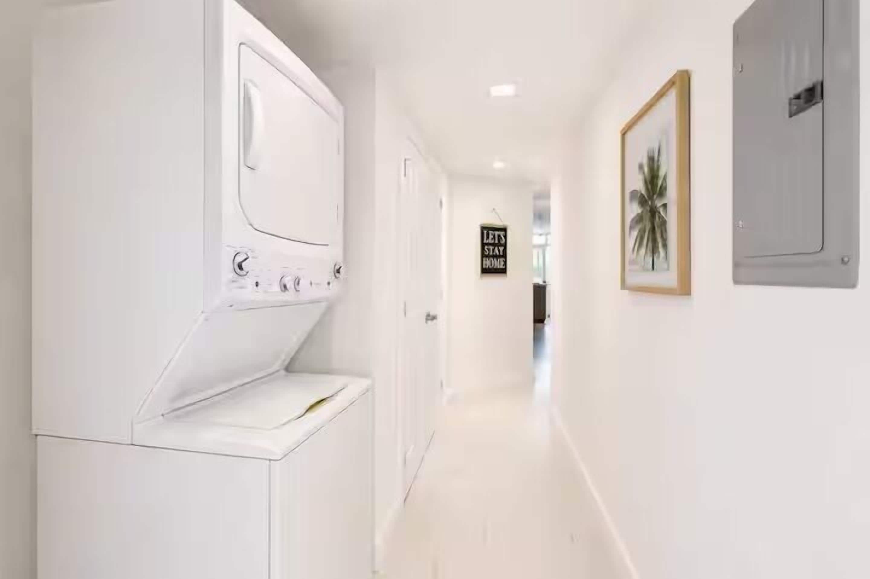 A laundry room with a washing machine, a dryer, and a sign that says 'LET'S STAY HOME'.