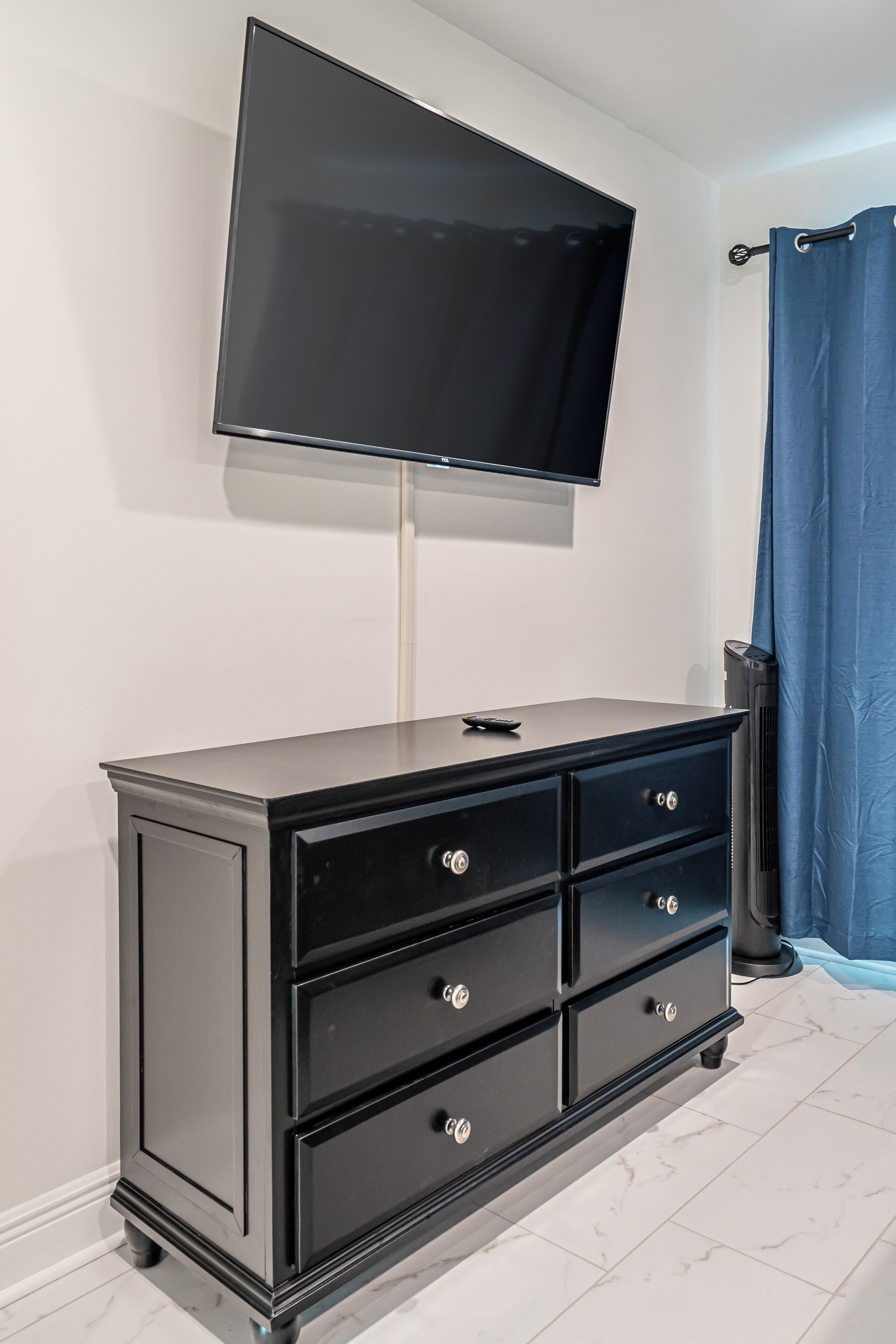 Ein modernes Zimmer mit einer schwarzen Kommode, einem an der Wand montierten Flachbildfernseher und einem blauen Vorhang.