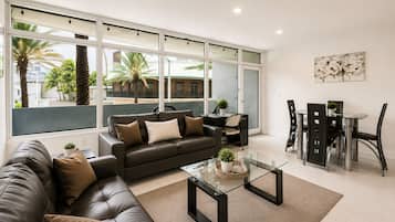 A modern living room with a leather sofa, a glass coffee table, and a dining area with a glass table and chairs.
