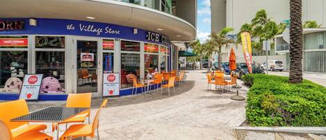 An outdoor seating area with orange chairs and tables in front of a store named 'The Village Store' with an 'ICE CREAM' sign.