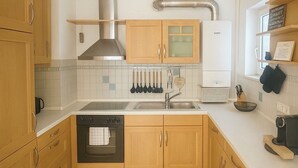 A kitchen with wooden cabinets, a stainless steel range hood, a built-in oven, a sink, and a coffee maker. - C&V: 5 PP- 3 rooms- central+WLAN+box spring bed (Kaiserslautern)
