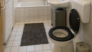 A modern bathroom with a bathtub, toilet, sink, and a small window. - C&V: 5 PP- 3 rooms- central+WLAN+box spring bed (Kaiserslautern)